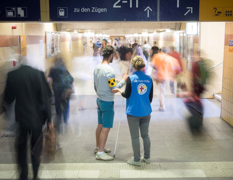 Mitarbeiterin der Bahnhofsmission hilft einer Person sich am Bahnhof zurechtzufinden